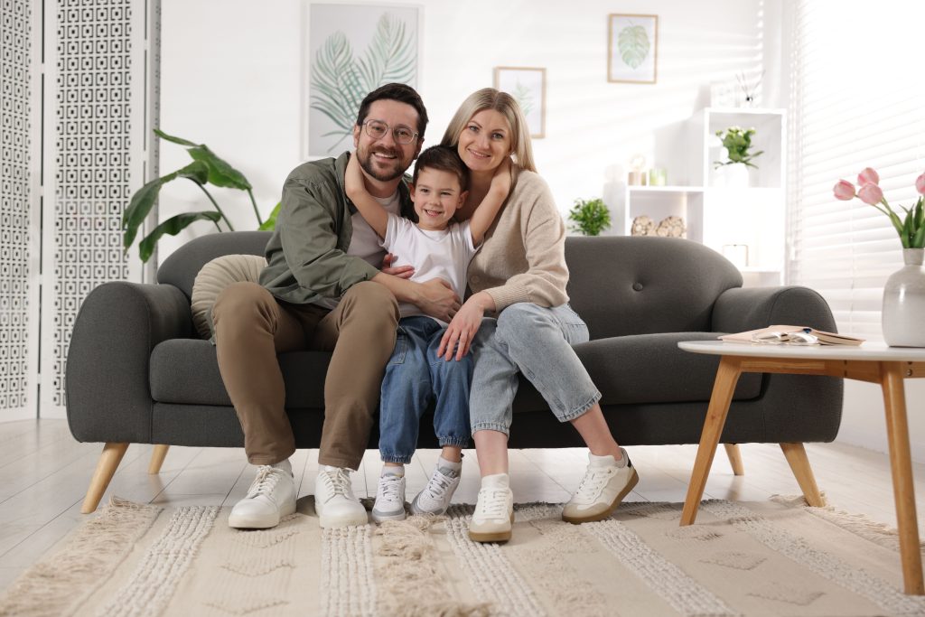 Happy family sitting together on a cozy sofa in a well-lit living room, showcasing a warm and inviting home atmosphere.