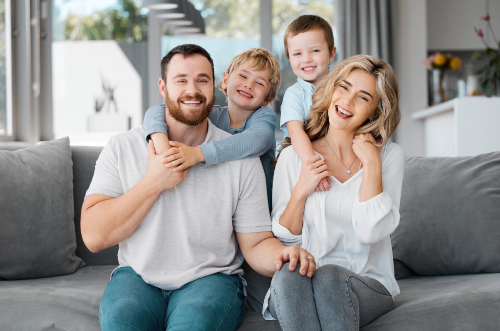 Smiling Caucasian family of four relaxing together on a couch, representing comfort and safety in a home environment, relevant to gas line maintenance and home safety services by Heat Busters in San Diego.